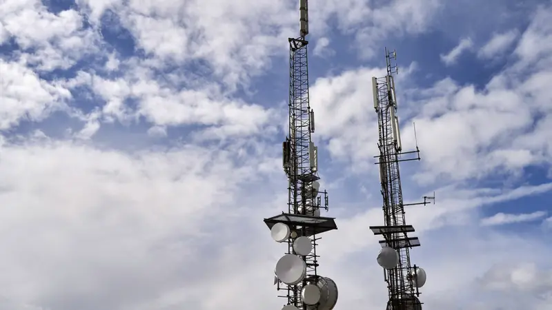 Deux pylônes de télécommunication couverts d'antennes et de paraboles sous un ciel nuageux