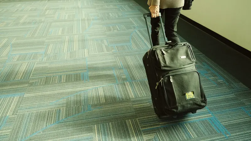Voyageur tirant une valise noire à roulettes dans un couloir d'aéroport à moquette bleue