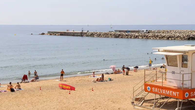 Plage de sable de Barcelone avec baigneurs, digue en enrochement et poste de secours orange