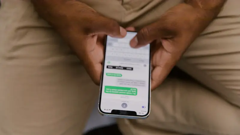 Smartphone tenu à deux mains, écran ouvert sur une conversation et le clavier