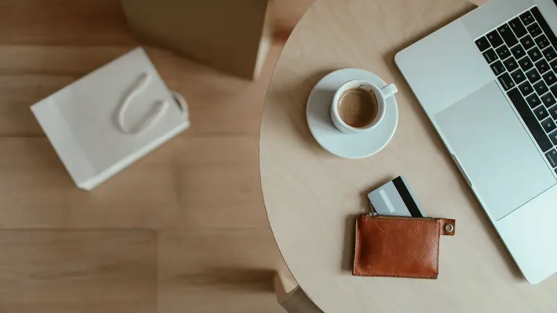 Vue du dessus d'un ordinateur portable ouvert sur une table ronde en bois, avec une tasse de café et un porte-cartes