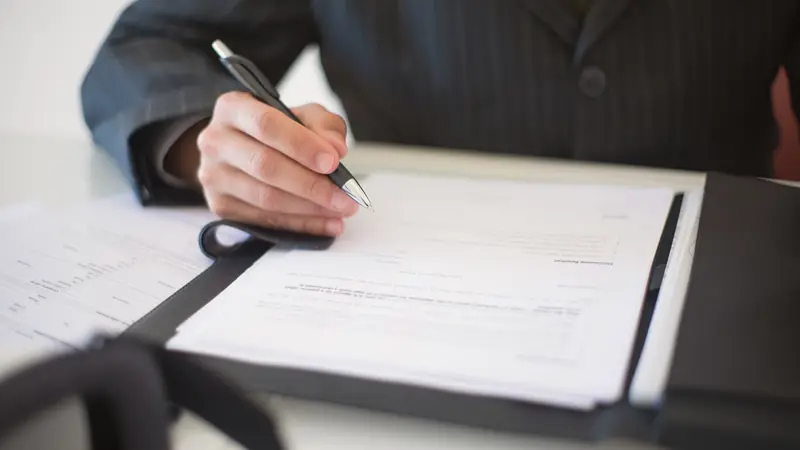 Main tenant un stylo au-dessus d'un contrat posé dans un porte-documents