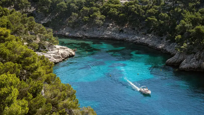 Calanque étroite aux eaux turquoise bordée de rochers calcaires blancs et de pins, un bateau à moteur au centre