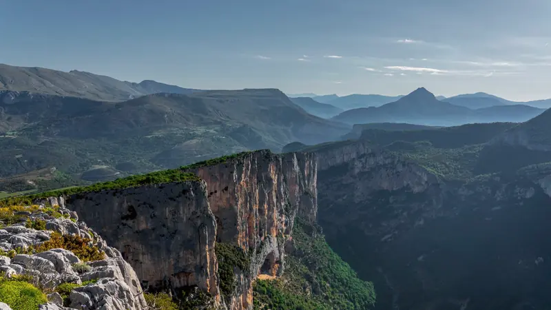 Parois calcaires orangées du canyon du Verdon vues depuis un rebord rocheux, montagnes à l'horizon