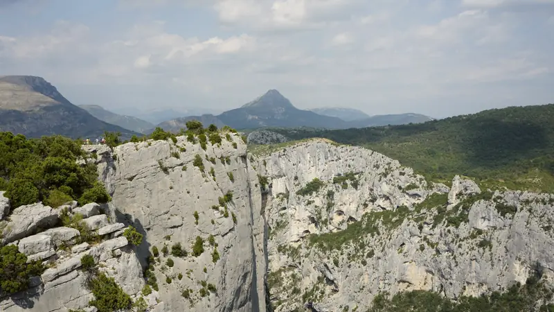 Visiteurs sur un belvédère au sommet d'une paroi grise des gorges du Verdon, face à un sommet pointu