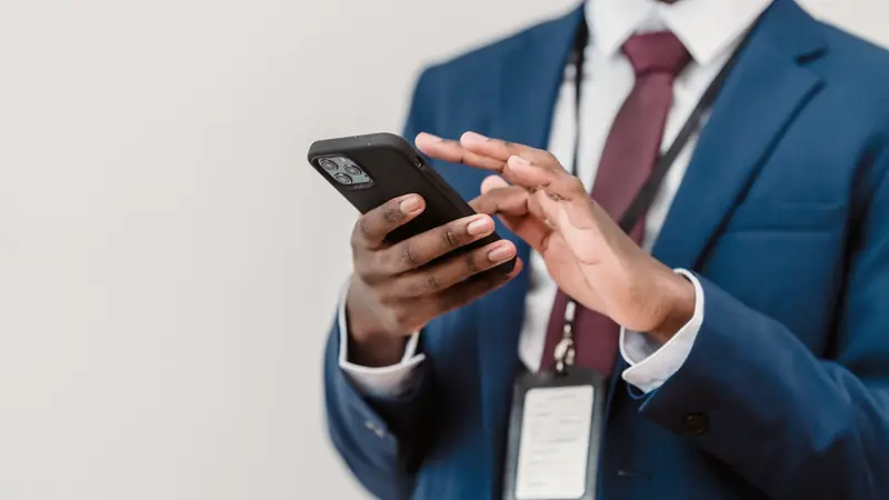 Homme en costume bleu et cravate bordeaux manipulant un smartphone à deux mains