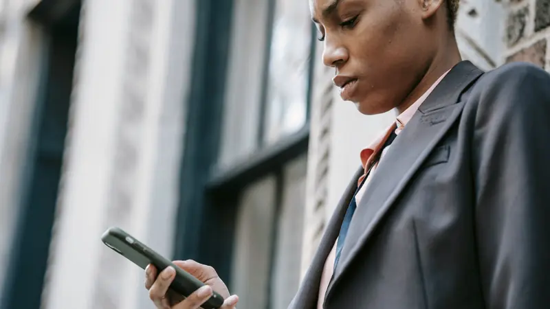 Femme en veste de tailleur consultant son smartphone devant une façade d'immeuble