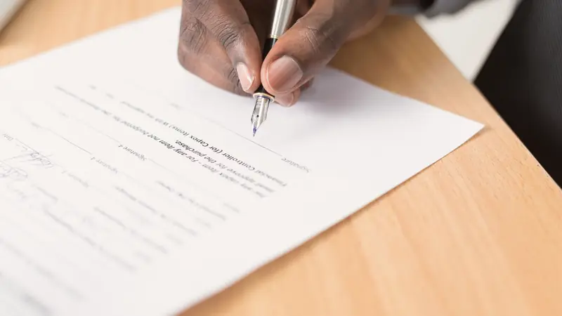 Main signant un contrat imprimé avec un stylo plume sur une table en bois