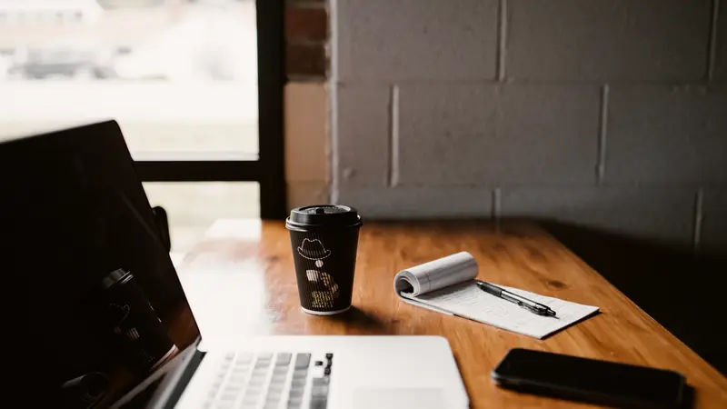 Ordinateur portable, café et bloc-notes sur un bureau en bois près d'une fenêtre