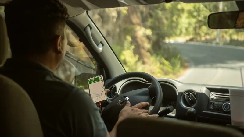 Conducteur suivant un itinéraire GPS affiché sur son téléphone, sur une route boisée