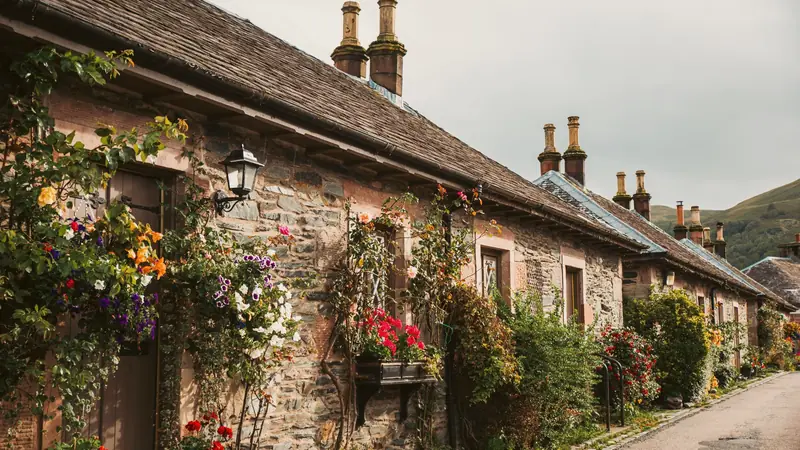 Rangée de maisons de village en pierre aux façades fleuries, au pied d'une colline