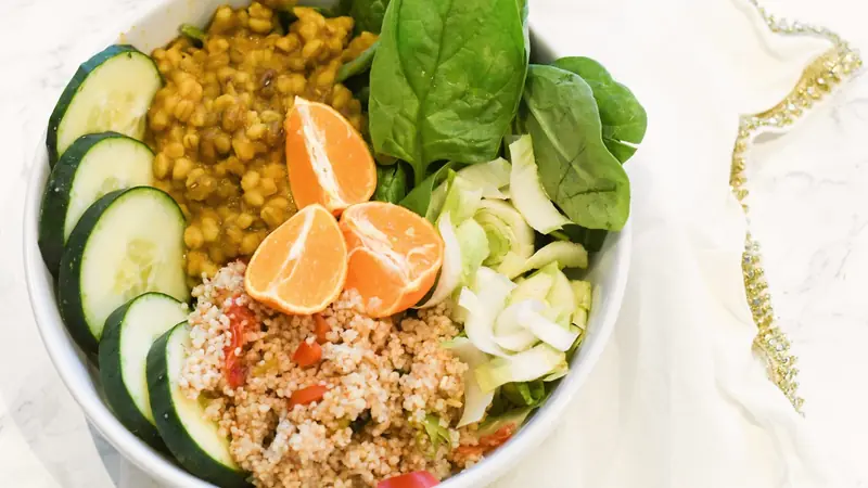 Bol de semoule de couscous aux légumes, lentilles en sauce, épinards, concombre et quartiers de mandarine