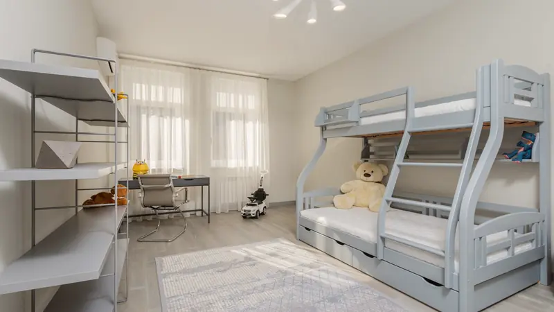Chambre d'enfant claire avec un lit superposé gris à échelle, des tiroirs sous le couchage et un bureau près de la fenêtre