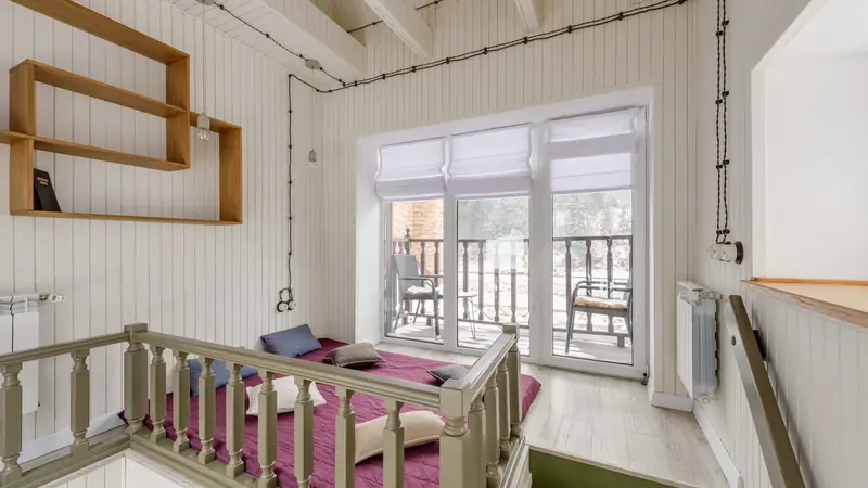 Couchage en mezzanine sous un toit lambrissé, matelas protégé par une balustrade en bois vert et accès par quelques marches
