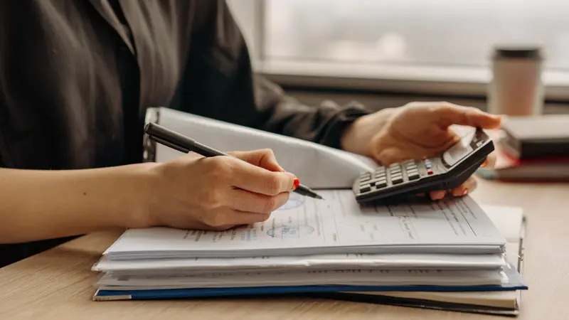 Mains remplissant des documents à côté d'une calculatrice sur un bureau
