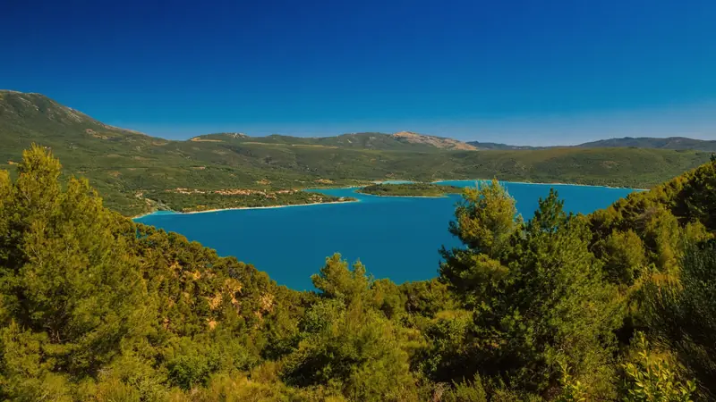 Lac turquoise bordé de pinèdes, avec une presqu'île et un village sur la rive, par temps clair