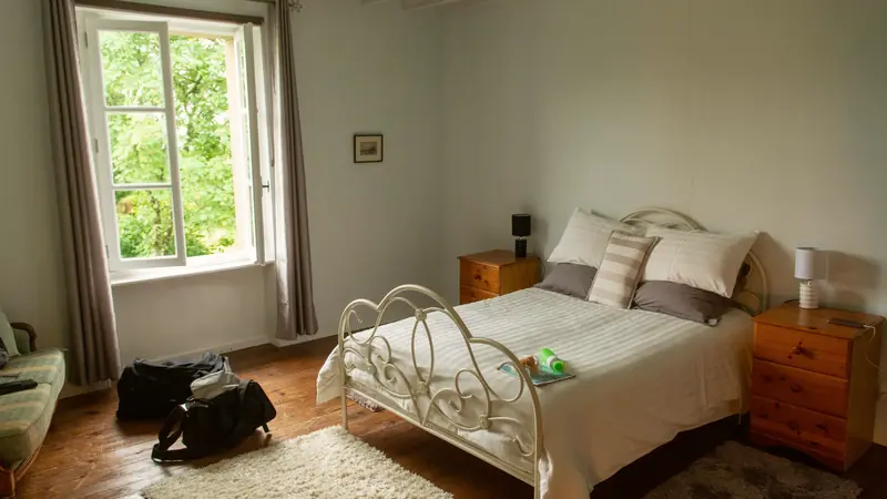 Chambre au parquet ancien avec lit en fer forgé et fenêtre ouverte sur la verdure