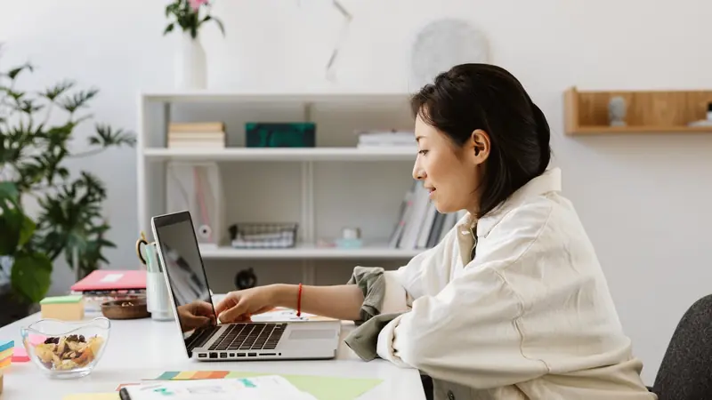 Femme assise à un bureau clair, en train d'utiliser un ordinateur portable
