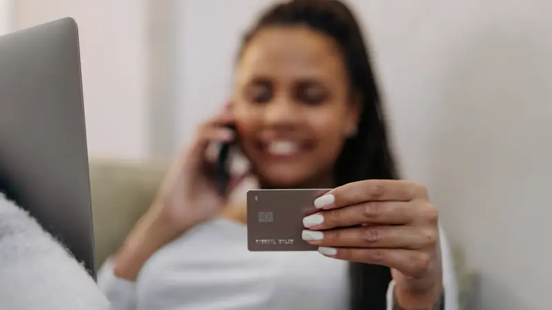 Femme au téléphone tenant une carte bancaire devant un ordinateur portable