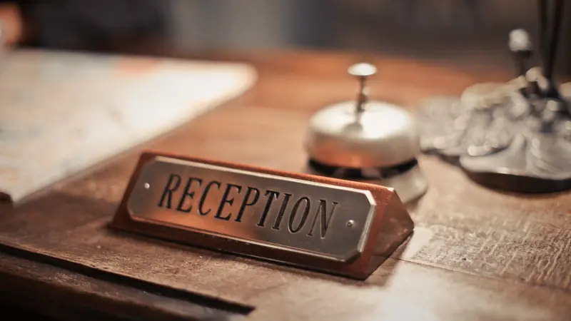 Plaque « Reception » et sonnette posées sur un comptoir d'accueil en bois