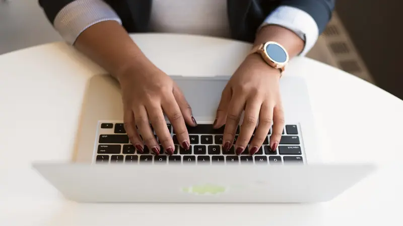 Mains d'une femme en veste sombre tapant sur le clavier d'un ordinateur portable gris, vues de dessus